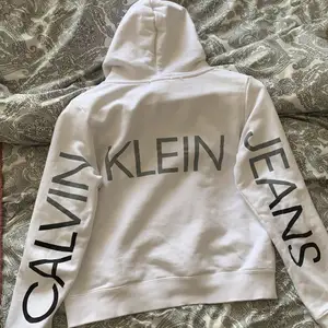 Vit Calvin Klein hoodie med tryck på ryggen! Köpt för 800kr, sparsamt använd. Stolek ”14” Allstå xs. Hitta en liten fläck (bild 3) men går säkert bort i tvätt🤍 plus frakt