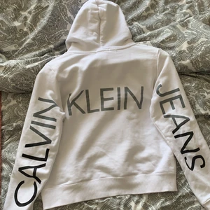 Calvin Klein hoodie  - Vit Calvin Klein hoodie med tryck på ryggen! Köpt för 800kr, sparsamt använd. Stolek ”14” Allstå xs. Hitta en liten fläck (bild 3) men går säkert bort i tvätt🤍 plus frakt