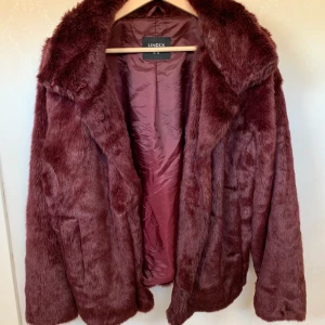 Vinröd fluffig jacka - Aldrig använd. Är en väldigt mysig jacka, har bara inte haft något som passar till denna fina jacka. Köparen står för frakten!