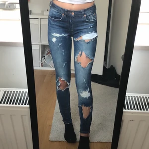 Slitna jeans - Lågmidjade slitna jeans från Ginatricot, i strl 25/30. Guldiga dragkedjor längst ner på benen som ej syns på bilderna. Endast använda 2-3 gånger.
