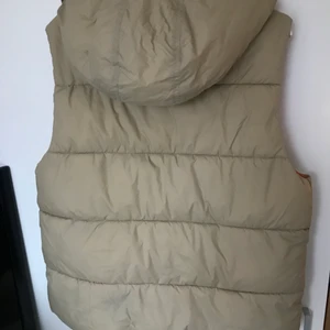 Beige dunväst - Beige dunväst med oranget innertyg. Avtagbar luva😁