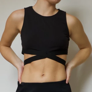 SVART TOPP MED BAND - Svart asskön topp med band kring revbenen! Storlek S.