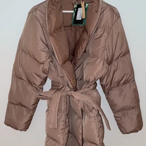 MQ Lana Puffer jacka Amphora, strl LARGE - Helt ny , oanvänd Lana puffer jacka! En stilren, vadderad jacka från Stockh lm. Jackan är en lätt a-linjeformad modell med sjalkrage och dold omlottknäppning med tryckknappar. Knytbälte i midjan för en smickrande siluett. Tyget är semi-matt för en lyxig känsla samt behandlad med BIONIC FINISH ECO för en regntålighet där höga krav på prestanda och hållbarhet tillgodoses.