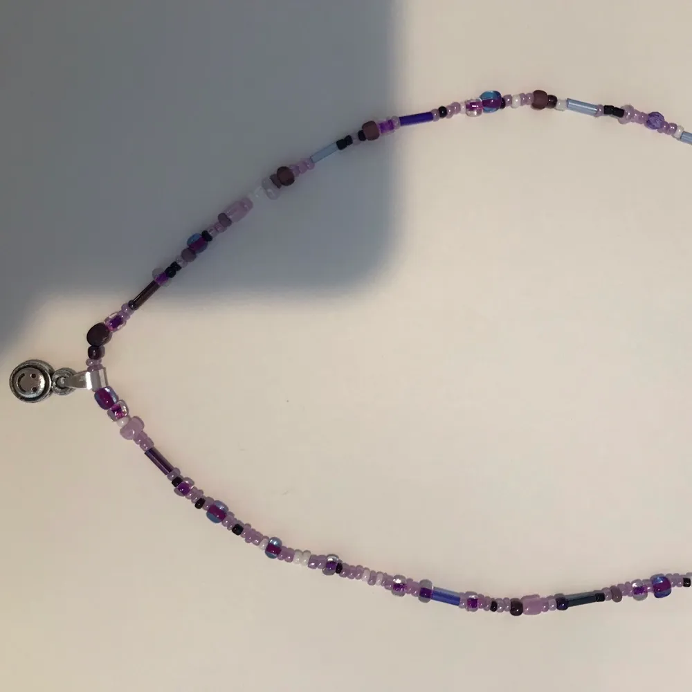 Ett gulligt halsband i olika lila nyanser med en silvrig  smiley😊 . Accessoarer.