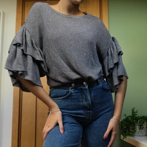 Silvrig festtröja med volanger  - Festlig blus/tröja som är stickad i ett silvrigt material🪙  Snygga stora volanger på ärmarna! Frakt ingår ej i angivet pris