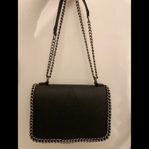 Svart skinnväska med kedja - En svart axelväska i skinnimitation med silverkedjor till både vardags och finare tillfällen! Helt oanvänd och i nyskick!✨👜 Inuti försluts väskan samt fack med dragkedja. 