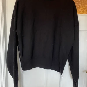 Svart stickad polotröja från other stori - Svart stickad polotröja från other stories. Ullmix. Tröjan har dragkedjor på sidorna nere vid mudden. Croppad modell. 