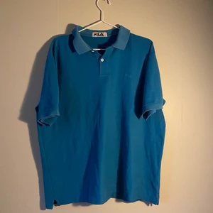 FILA piké  - En blå FILA piké köpte second hand men i gott skick. Piken är i storlek XXL men skulle säga att den sitter mer som en XL. Två knappar vid kragen.