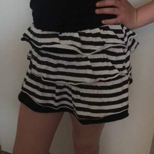 Kort kjol med tre volanger i svartvit randigt och shorts under.
