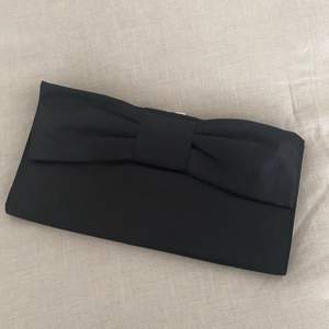 Söt, stel kuvertväska med svart rosett i lätt glansigt material. Använd två kvällar. I väskan finns hållare för kedja som du kan koppla på om du har en eller köper till. 