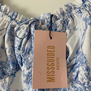 Vit klänning med blått mönster - Helt ny klänning som tyvärr var för stor. Storlek 32. Prislappen sitter kvar. Köpte den för 500kr. 