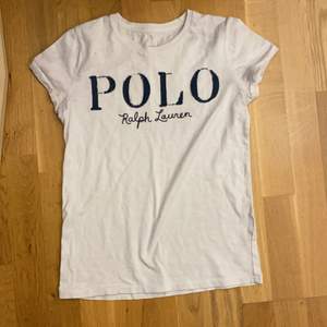 En vit Polo Ralph Lauren T-shirt. Använd ett part gånger för ca 3/4 år. Vit/beige aktig färg med blå text.
