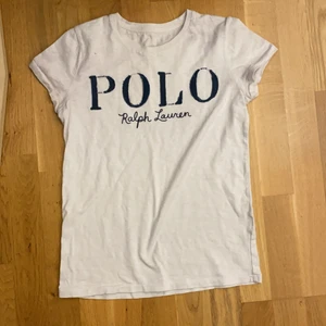 en vit t-shirt, Storlek XS - En vit Polo Ralph Lauren T-shirt. Använd ett part gånger för ca 3/4 år. Vit/beige aktig färg med blå text.