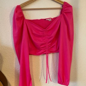 Rosa kropptopp med ”ruffle” - Rosa kropptopp med långa armar och justerbar framsida.