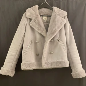 Ljusgrå supermysig jacka  - Ljusgrå jacka i mockaimitation och fuskpäls och silvriga detaljer. Knapparna går inte att stänga men fickorna är rymliga. Super mjuk och varm. Storlek 10 från River island. O mycket gott skick