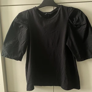 Svart tischa med puffärmar - Längre ärmar med snygg puff vid axlarna. Själva tröjan är vanligt t-shirt material medan ärmarna är lite tunnare tyg. Fint skick. 