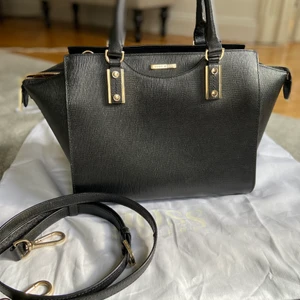 Hugo Boss Maika Handväska - Elegant handväska från Hugo Boss i fin struktur läder med gulddetaljer. Tvåvägs blixtlås med stort utrymme. Tillhörande axelrem och dust bag.  Tidlös och business casual looks.  Storlek 34x25x18 cm   Ordinarie pris 5499 kr inköpt på NK.  Hämtas på Östermalm 