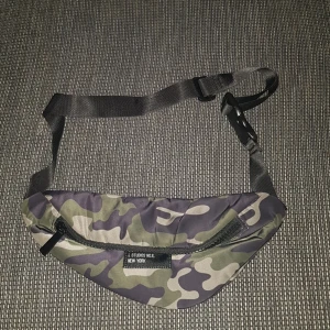 NEW YORKER Magväska - Magväska man kan ha den runt sig hur man vill och man kan göra den större och mindre. Är i Camo färg. Köparen står för frakt.