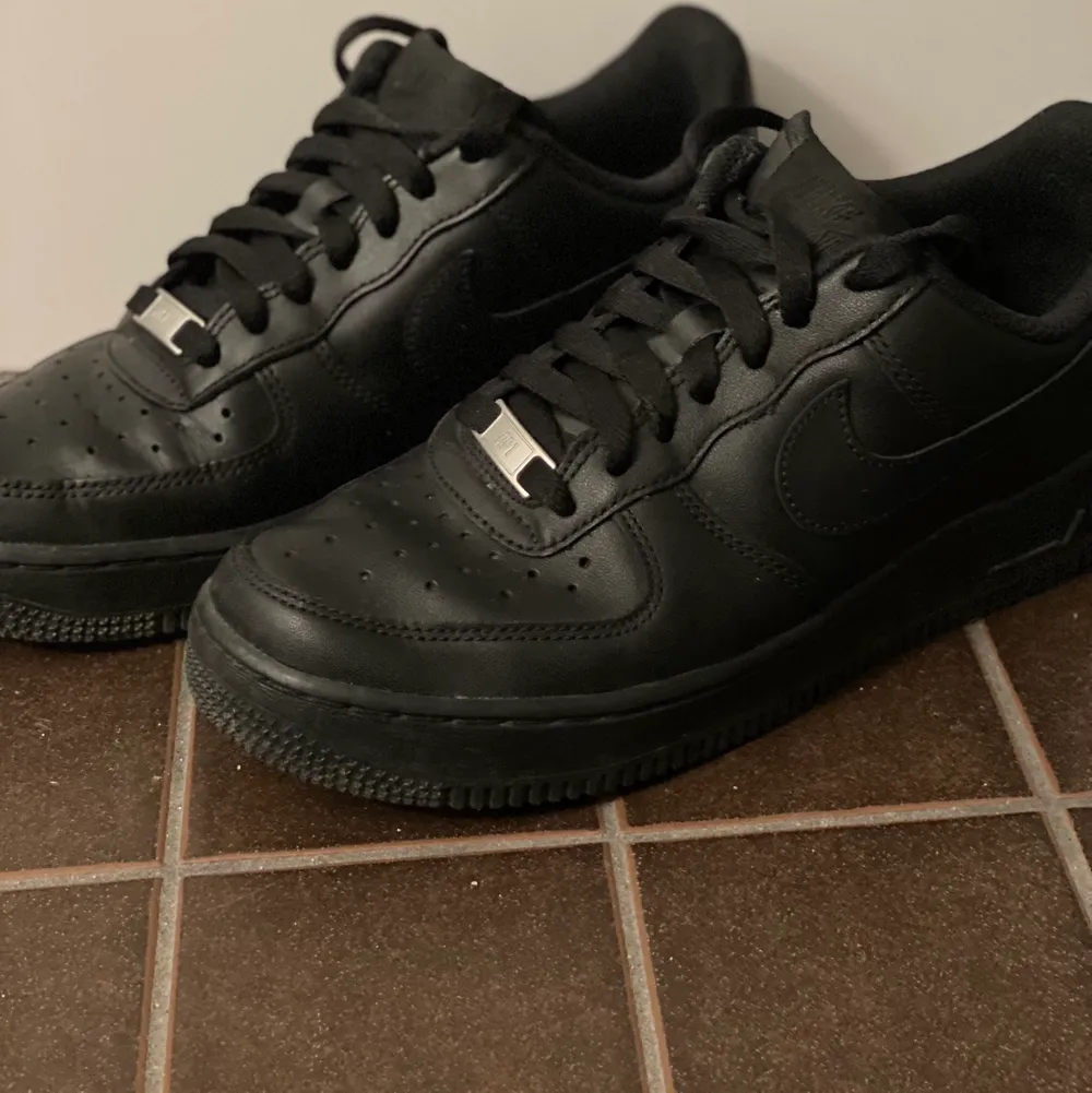 Nike Air Force 1 Low-sneakers. Ovandelen är gjord i svart läder och Nikes ikoniska Swoosh är placerad på skornas sidor. Sulan är utrustad med den revolutionerande Air-enheten som ger optimal stötdämpning. Svarta i storlek 38,5. Skor.