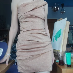Festklänning - Glitrig tight klänning med en off theshoulder shoulder. Vrinkeldetaljer. Textilen är i rosigbeige med guldglitter. Står small 36 i den. (Hehe ignorera att galjloopen hänger ut)