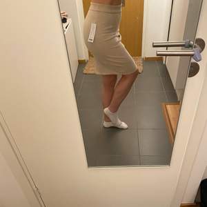 Oanvänd Beige kjol i mockaimitation med dragkedja i ryggen, jag är 160 cm och den går till knäna. Köparen betalar frakten 