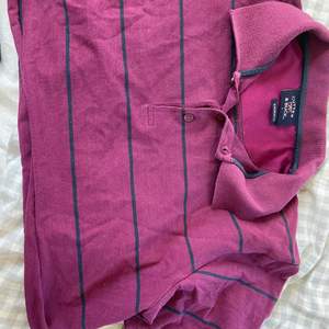 Vinröd/lila polo T-shirt med mörkt marinblå tunna ränder, den är kroppad vid midjan så den passar bra till bla högmidjade byxor/kjol. 20kr+frakt