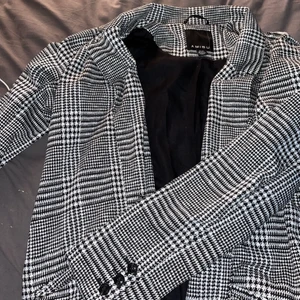 Hundtandsmönstrad kappa - Lång kappa från New Yorker i storlek 38. Bara legat i en garderob så inte använd. Skriv för fler bilder!