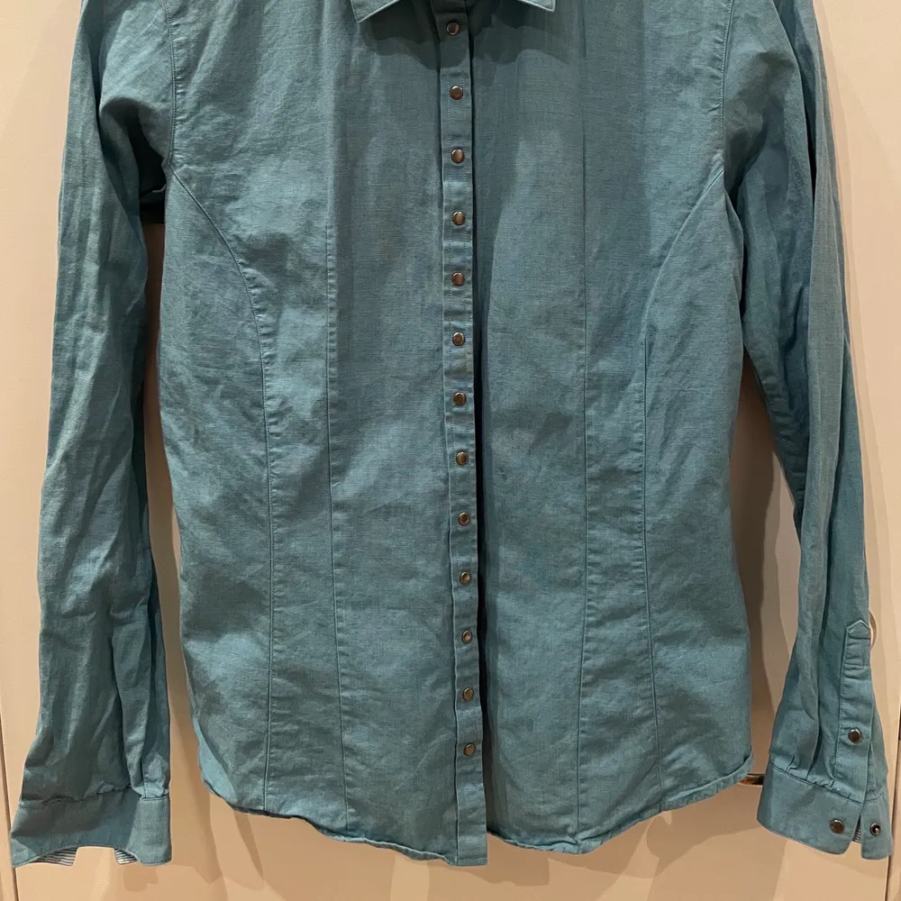 Blå skjorta i fint skick från The Shirt Factory i storlek 36 med tryckknappar.. Skjortor.