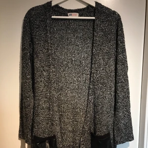 Grå kofta med fickor av konstläder - Stickad kofta i mörkare grå, från H&M. Två svarta fickor i konstläder. Den är i barnstorleken 158/164 men passar som en S. 