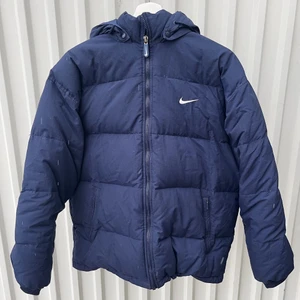 NIKE Dunjacka - Marinblå dunjacka från NIKE i storlek M, unisex. Avtagbar luva. Fint skick, inga defekter. Skickas spårbart via PostNord.  Mått:  Längd: 65 cm Bredd: 55 cm Arm: 55 cm