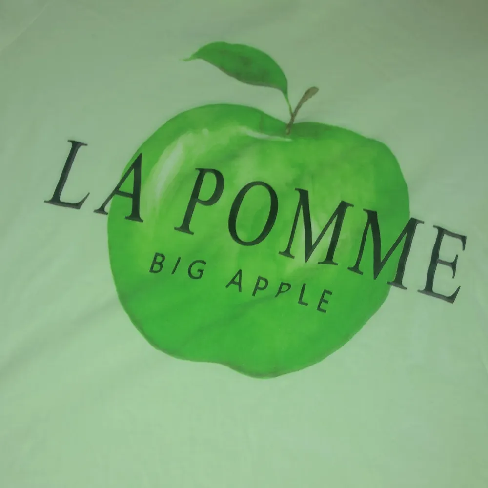 En vit t-shorts med ett grönt äpple och texten:            (la pomme). T-shirts.