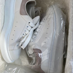 Alexander McQueen oversized sneakers - Jag har bestämt mig för att sälja mina Alexander McQueen sneakers i storlek 38 1/2.  De är gjorda i vitt läder och har en hälkåpa i ljusrosa mocka. De är köpta förra våren på NK access i Stockholm och är så gott som nya. Orginalkvitto, äkthetsbevis och originalbox finns. Skriv för fler bilder! Köparen står för frakten!
