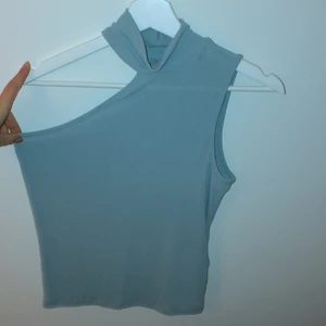 Topp - Turkos/grå topp från Gina Tricot. Hög hals och bara en arm. Är i storlek M men passar även mindre och större pga stretch. Använd fåtal gånger så är i bra skick. Köpt för 200kr. Köparen står för leveransen och betalning sker via swish!💕