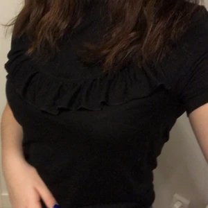 Svart t-shirt med volang - Svart t-shirt med en volang tvärs över bröstet, supermysig tröja och väldigt mjukt material.