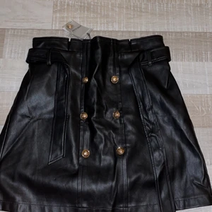 Skinkjol - Skinkjol från River Island med brons/guld färgade knappar. Aldrig använd med prislappen och en extra knapp kvar. Tyvärr är den för stor på mig annars hade jag lätt använt den! Går att knyta med bältet men går även att ta av. Ursprungspris:350kr