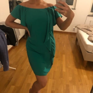 Vila klänning, M - Turkos/grön (mycket härlig färg) klänning i storlek M från Vila. Den har snyggt ”fall” av tyg på ena sidan. Sitter mer löst men går att använda bälte ifall man skulle vilja främja midjan mer. Använd 1 gång. 