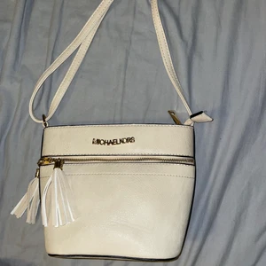 Michael Kors väska - OBS! Inte äkta. Michael Kors axelrems väska i beige/vit färg. Större utrymme med två små innefickor, en med dragkedja. Väskan är justerbar, väldigt praktisk och rymmer en del! 