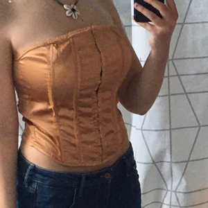 Bronsfärgad korsett - Strechig korsettliknande topp med små spännen lånat fram. Den toppen är formad så att den är tightare runt midjan och lösare vid bysten. Storlek M