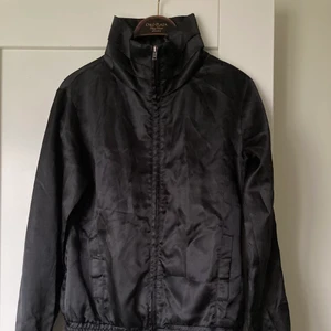 Svart jacka med ståkrage - En svart glansig jacka med ståkrage och mudd nertill. Använd ett fåtal gånger. Storlek M. 