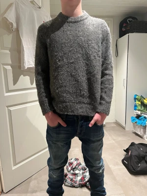 Grå stickad tröja från H&M - Mysig grå stickad tröja från H&M i relaxed fit. Tröjan har rund halsringning, långa ärmar och är tillverkad i ett mjukt, grovstickat material. Perfekt för kalla dagar och enkel att matcha med jeans eller kjol.