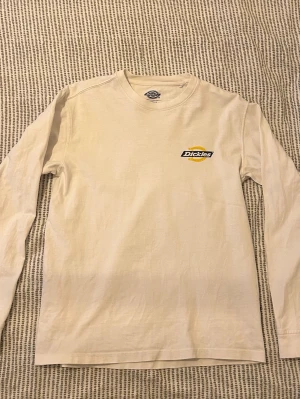 Vit långärmad Dickies t-shirt - Säljer en vit långärmad t-shirt från Dickies med klassisk logga i gult och svart på bröstet och ryggen. Bra skick, inga hål. Normal passform. Passar mig som är 174.