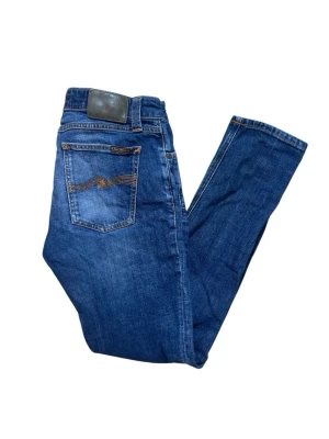 Blå jeans från Nudie Jeans - Snygga blå jeans från Nudie Jeans med klassisk femficksmodell och kontrastsömmar sop syns på bakfickan. Jeansen har normal passform och är tillverkade i slitstarkt bomullsdenim. Perfekta för dig som gillar en enkel men stilren look. Sitter tight