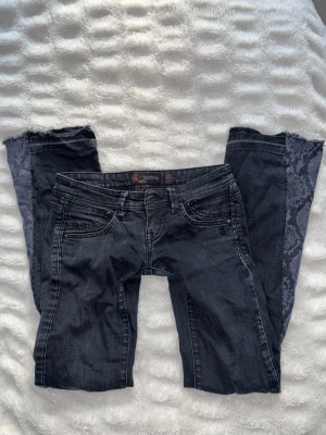 Svarta väldigt lågmidjade bootcut jeans  - Unika svarta jeans från Mogul (?) som jag har sytt om med symaskin till bootcut med ormskinn mönster där nere. De är väldigt lågmidjade (se dragkedjan). Passar storlek 27/32. Rätt bra skick men notera att jag sytt själv ! Har ett litet hål på knät som ska vara där