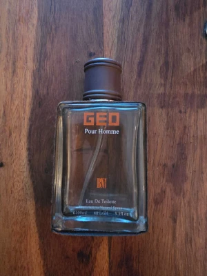GEO Pour Homme Eau De Toilette - Maskulin parfym GEO Pour Homme från BN Parfums. Flaskan är fyrkantig i genomskinligt glas med brunt lock och detaljer. Texten på flaskan är orange och vit. Innehåller 100 ml Eau De Toilette med sprayfunktion.