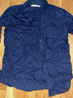 Mörkblå skjorta med bröstficka - En enkel mörkblå skjorta med klassisk krage och bröstficka. Skjortan har knappar framtill och är långärmad. Perfekt till jeans eller chinos för en clean look.