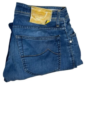 Blå jeans från Jacob Cohen - Snygga blå jeans från Jacob Cohen med klassisk femficksdesign och guldfärgad patch med J-logga bak. Jeansen har raka ben och är tillverkade i mjukt denimtyg med diskreta slitningar. Perfekta för en avslappnad och trendig look.