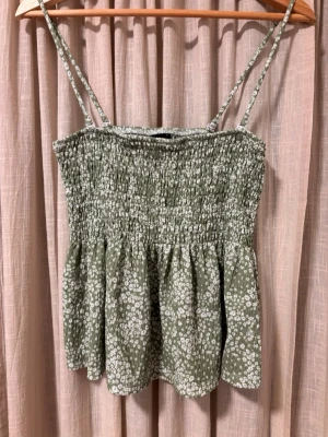 Grönt blommigt linne Gina Tricot - Supersöt grönt linne från Gina Tricot med vita små blommor. Tunna axelband och en lätt volang nedtill.