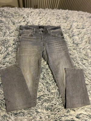 Gråa slim fit jeans från Jack & Jones - Snygga gråa slim fit jeans från Jack & Jones med klassisk femficksdesign och diskreta slitningar. Jeansen har normal midja, dragkedjegylf och är tillverkade i mjukt denimtyg som ger en bekväm passform.