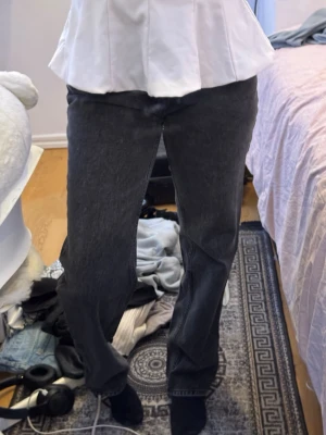 Svarta raka jeans med hög midja - Säljer ett par svarta raka jeans med hög midja och klassisk femficksdesign. Jeansen har en avslappnad passform och är tillverkade i ett kraftigare denimtyg. Perfekta för dig som gillar en enkel och stilren look.