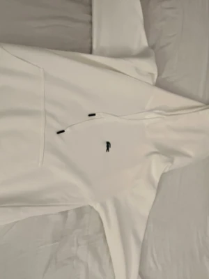 Vit hoodie från Lacoste med logga - Snygg vit hoodie från Lacoste med klassisk krokodillogga broderad på bröstet. Hoodien har huva med dragsko och en stor magficka framtill. Perfekt för en clean och stilren look.